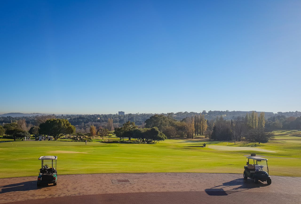 Home A panoramic view of a golf course with golf carts under a clear blue sky on a sunny day.