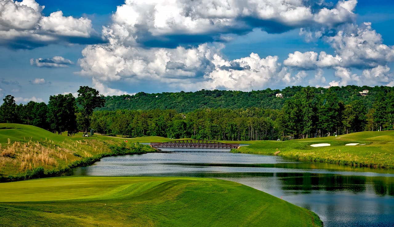 Home Scenic golf course with lush greenery, river, and a bridge under a bright summer sky.